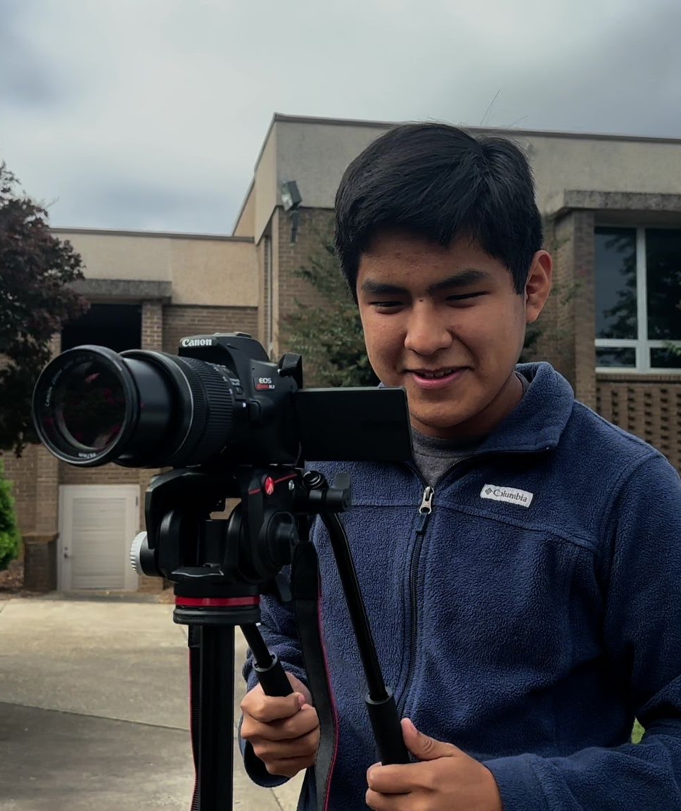 Sam recording the school's promotional video. He is holding a DSLR Camera